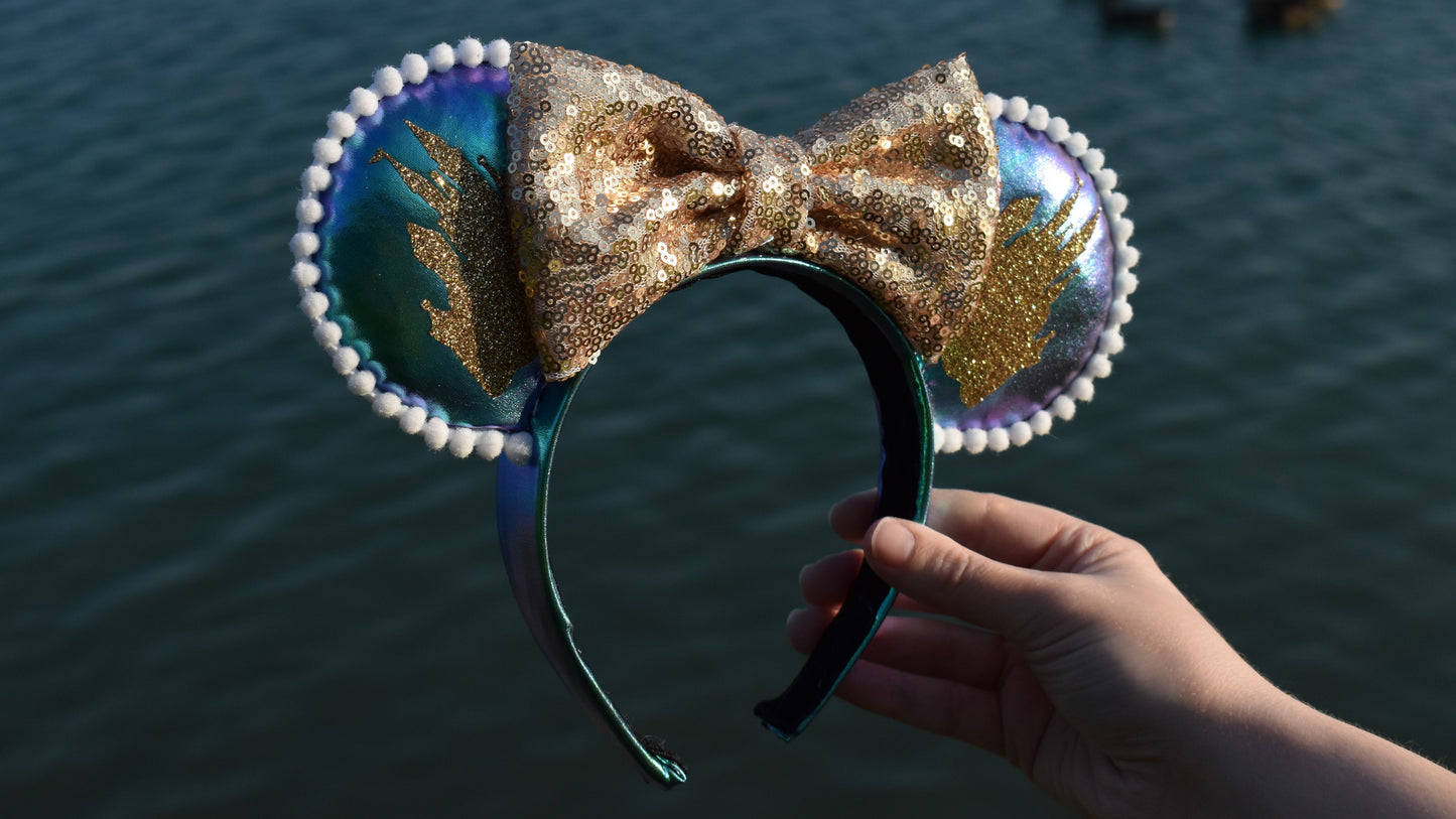 Iridescent purple and blue Disney ears with gold glitter Cinderella's castles on both front and back, with a white pom pom trim on each ear and a gold sequin bow.